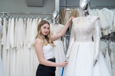 A pretty sales consultant measures a wedding dress for a client and shows impeccable quality. Bridal store