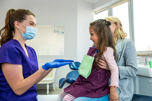 dentist woman in medical clothes checks teeth of baby girl to avoid caries. The concept of dentistry in dentistry