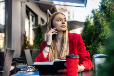 Young woman enjoying coffee sitting on the terrace of a cafe on the street of a modern city. A man sits at a table and uses a laptop outdoors.
