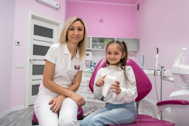 small patient sits in the dentist's chair where the dentist tells her how to brush her teeth correctly. the concept of treatment of children's teeth.