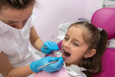 beautiful little female patient grimaces during an examination of the oral cavity by a female dentist. toothache in children. oral health