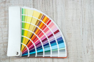 Masanın üzerinde parlak renk paleti kataloğu var. Grafik tasarımcısı örnekleyicideki renkleri seçer