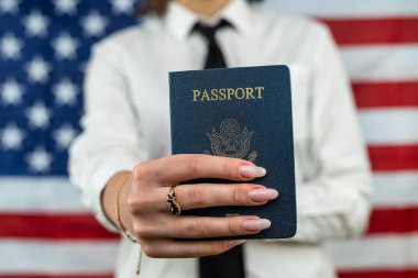 cropped portrait of a young flight attendant holding a fan of dollars and an American passport and standing against an American flag background. travel passport control