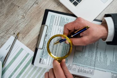 Male hand using magnifying glass and work with 1040 tax form, legal business contract. Accounting concept