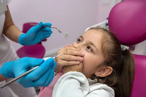 little patient covers her mouth with her hands and does not allow the dentist to look into her mouth. fear of the dentist. the child is afraid dentistry