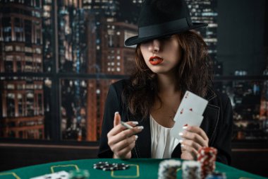 woman's hand takes poker cards at a round poker table. risky bets in poker. casino. a woman in a hat