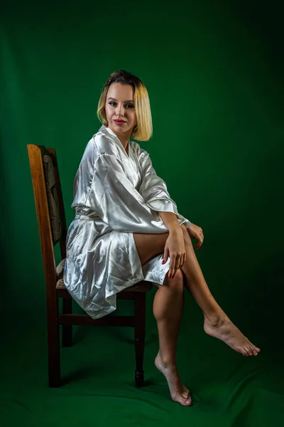 スタジオの木製の椅子に座っている絹のローブを着た若い魅力的な女性の肖像画 緑の背景に隔離された 肖像写真の概念です フレームの中の美しい女の子 — ストック写真