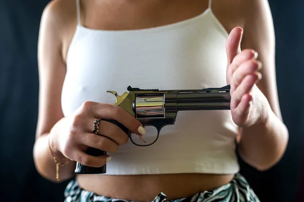 serious woman in stylish clothes posing faceless with revolver gun isolated on black background. shooting with a gun. a woman with a killer weapon