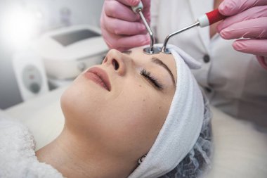 Güzellik uzmanı spa salonunda elektriksel impulslarla yüz işlemleri yapıyor. Cilt bakım spa konsepti