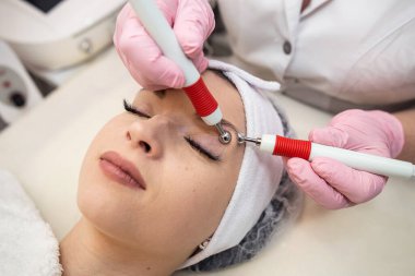 Genç ve güzel bir kadın spa kliniğindeki terapistten canlandırıcı bir yüz bakımı alıyor. Yüz gerdirme prosedürü