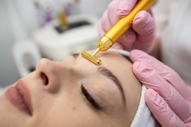 Kadın kaplıcada nabız yüz masajı yaptırıyor, kadın yüzünde titreşimli altın yüz masajı, gençleştirme prosedürü. Yüz derisi kavramı gençlik dolu ve sağlıklı.
