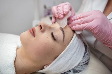 Güzel bir kadın güzellik kliniğinde guasha tedavisi ile yüz masajı yaptırıyor. Sağlıklı yaşam tarzı