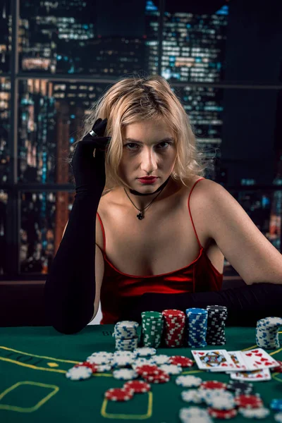赤いイブニングドレスの感情的な若い女性はカジノの緑の布のテーブルでトランプをしている 女はポーカーをする 赤いドレス — ストック写真