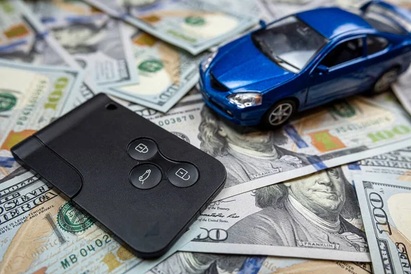 Blue samll toy car with real car keys lying dollar cash. Expensive gift. Sell or rent concept