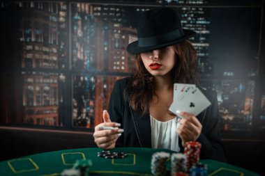 woman's hand takes poker cards at a round poker table. risky bets in poker. casino. a woman in a hat