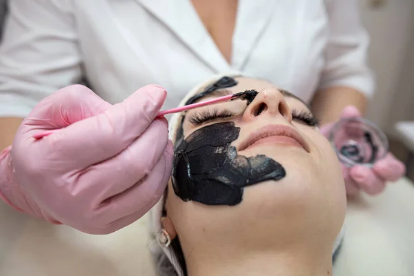 Cosmetologo Applicando Maschera Crema Nera Sul Viso Suo Cliente Trattamento — Foto Stock