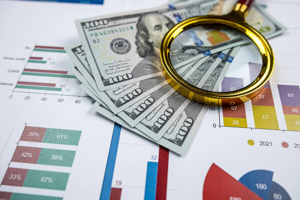 closeup of Magnifying glass dollar and pen on business charts graphs paper. Saving and accounting concept