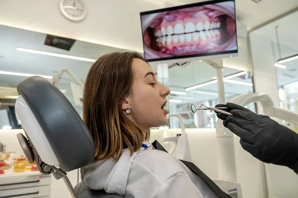 Over-the-shoulder view of a dentist examining the teeth of a girl patient in a dental clinic. A woman examines her teeth at a dentist.