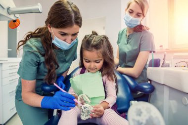 Diş hekimi, çocuk hastaya klinikteki minyatür çenelerde diş fırçasını nasıl kullanacağını gösteriyor. Sağlık Hizmetleri  