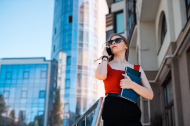 A beautiful business woman with a mobile phone is walking in the buildings in the city center. Woman and smartphone concept.