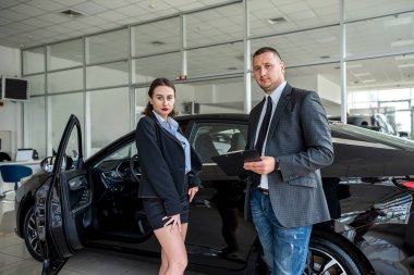  salesman showing a new modern car to the happy caucasian female client in showrom