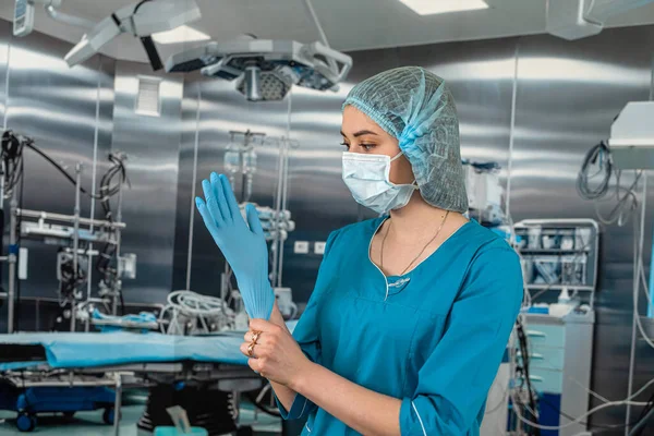 stock image doctor or nurse in a blue coat puts on blue rubber gloves prepares to examine a patient in the operating room. medicine. operating room doctor