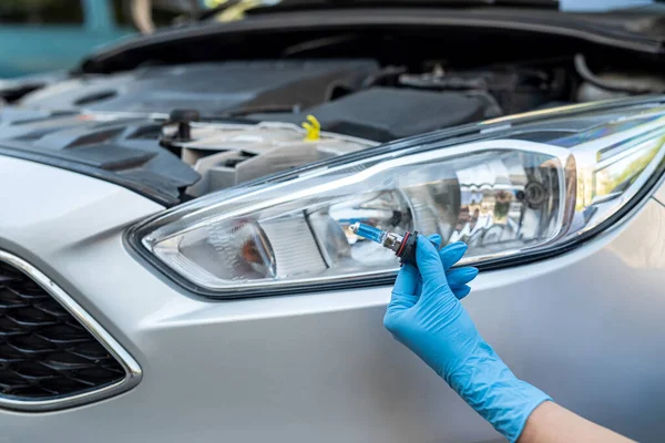 Close-up photo of a man\'s hands holding a car light bulb near the car for replacement. car repair lamp replacement or exchange. car headlight
