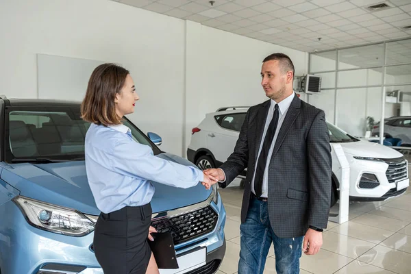 young pretty client shaking hands with man sales dealer in modern car showroom, success deal. concept of purchase vehicle