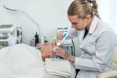 Güzellik salonundaki bir müşterinin yüzüne nemlendirici bir maske yapan bir güzellik uzmanının en iyi görüntüsü. Kozmetik bilimi kavramı.