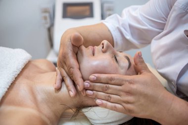 high angle view of massage therapist massaging the face of a brunette client with closed eyes. spa salon facial massage