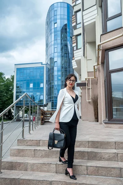 business career woman in business clothes goes to the office with a folder with documents on the background of a large building. Portrait of a successful business woman near the business center. The woman is the boss