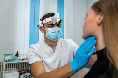 Doktor boğazını kontrol etmek için ağzını açan bir kadın hastanın boğazını muayene ediyor. ilaç.