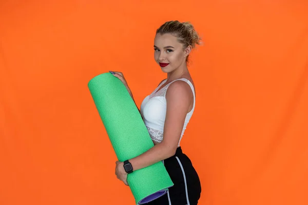 girl fitness trainer in sports shorts holds a mat for sports on an orange background. Sport is life concept. Women in sports