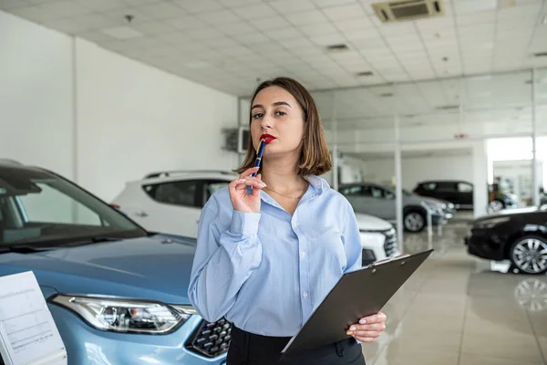 Stock image female dealer near new modern car holding tablet at showroom, sale concept 