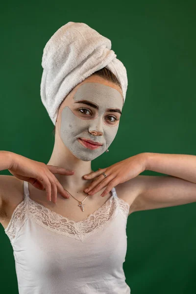 young woman applying green clay mask isolated on green. Beauty treatment, anti aging procedures