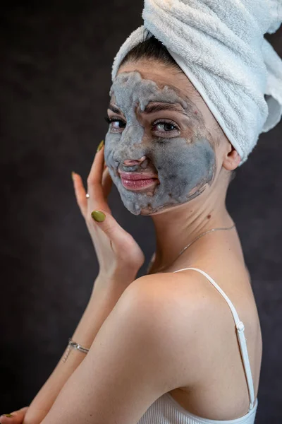 Female face with cosmetics cleansing gray bubble mask on dblack background. Anti aging treatment, skin care