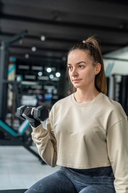 Eğitimdeki kız ağır ağır dambıllar ve tren kolları dayanıklıdır. Dambılı eller, yaklaşın. Spor kadını