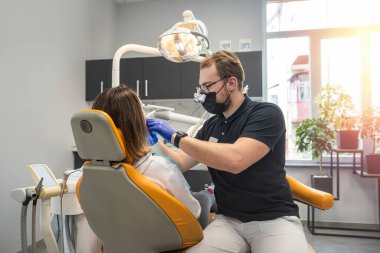 Dişçi modern bir diş muayenehanesinde bir hastanın dişlerini muayene eder. Kapatın. Tek kullanımlık tıbbi maske takan bir doktor. Anestezi için ağrı kesici enjeksiyonu.