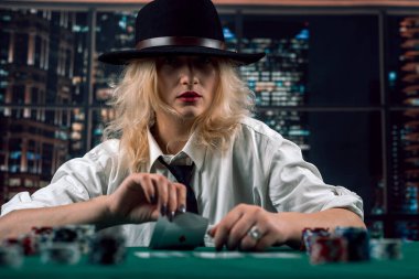 Kumarhanede elinde poker kartları tutan tişörtlü ve şapkalı çekici bir kız. poker. bayan oyuncu