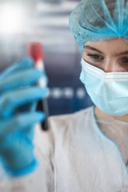 Koruyucu giysi tutan kadın bilim adamı klinik laboratuarında kan test tüplerini analiz ediyor. Kavram