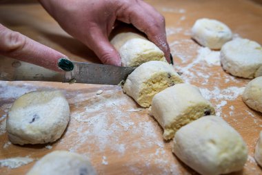 professional baker with knife cuts the raw sausage dough into even small pieces, making cheese cakes, a Ukrainian national dish