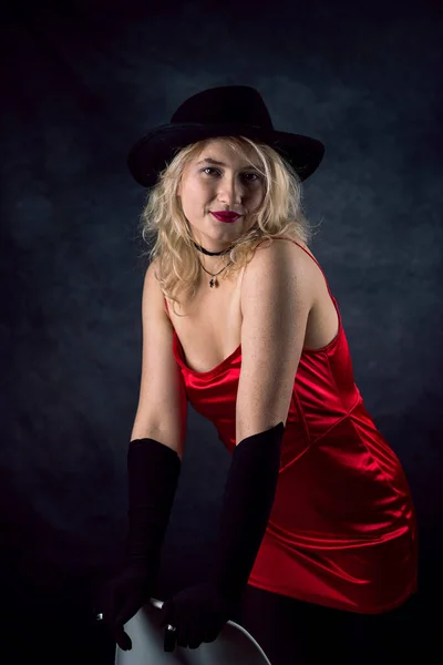 stock image pretty young blond woman wear red evening dress and black hat isolated on dark background. lifestyle