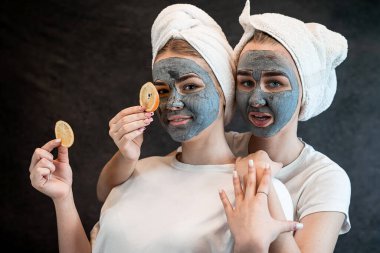 İki güzel kız ya da kız arkadaş siyah kilden güzel bir maske takıyor ve siyah üzerinde turuncu parçalar tutuyor. Vitamin maskesi derisi, spa prosedürü