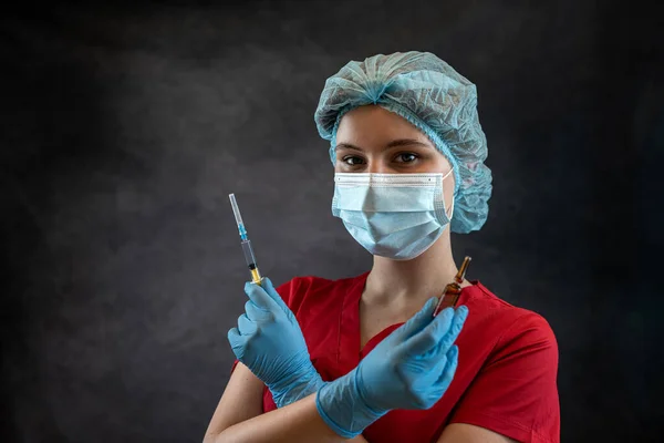 stock image Woman doctor in red medical coat holds a syringe for injections against coronavirus isolated on dark. Vaccination concept