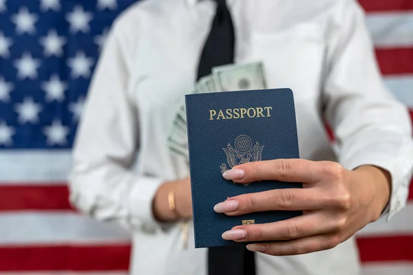 cropped portrait of a young flight attendant holding a fan of dollars and an American passport and standing against an American flag background. travel passport control