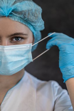 Genç hemşirelerin portresi bireysel koruma altında beyaz üniforma, eldiven gözlüğü ve koyu arka planda izole edilmiş şapkalar giyer. Sağlık hizmetleri kavramı