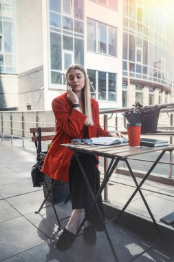 Ceketli genç bir kadın terasta bir kafede netbook üzerinde çalışıyor. Sonbahar sabahı. Sokak tarzı.