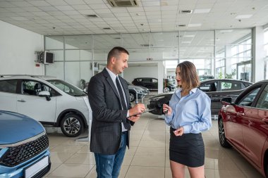 Bir araba galerisindeki erkek bir müşteriye tavsiye veren genç bir satış danışmanı. Yeni bir araba seçmek ya da almak. araba galerisi