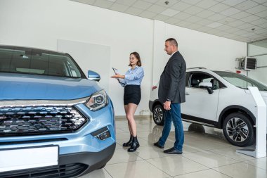 pretty young male shop assistant in suit talking with female client and helping choose it before buying dream auto in showroom 