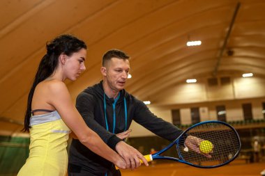 Genç erkek tenisçi bir kadına kortta tenis oynamayı öğretir. Tenis kortunda ellerinde raket olan bir çift. spor